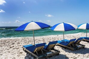 Ein Strand mit blauen und weißen Streifen-Schirmen und Holzliegen.