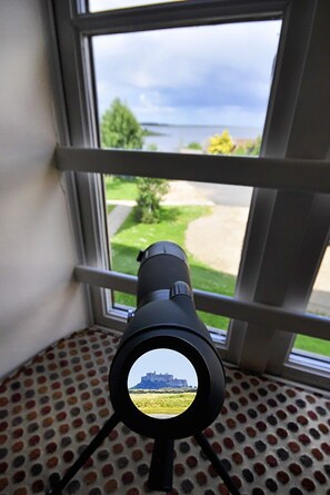 A telescope positioned against a window with a view of a grassy area and a distant building. - Bay View @ Waren Mill - North East Escapes (Waren Mill)