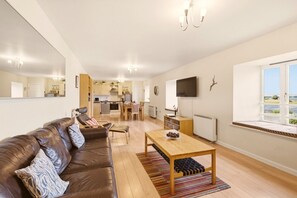 A modern living room with a leather sofa, a wooden coffee table, and a view of the kitchen and dining area. - Bay View @ Waren Mill - North East Escapes (Waren Mill)