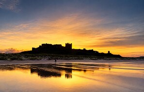 A castle on a hill with a beach in the foreground. - Bay View @ Waren Mill - North East Escapes (Waren Mill)