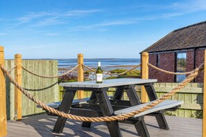 Eine Holzterrasse mit Tisch, Bänken, Seilen und einer Weinflasche.