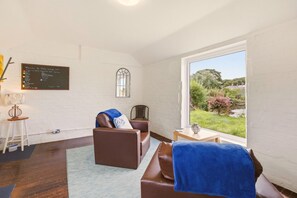 A room with a large window, a brown leather sofa, a small table, and a chair. - Bay View @ Waren Mill - North East Escapes (Waren Mill)