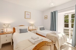 Ein Hotelzimmer mit zwei Betten, Nachttischen, Lampen und einem großen Fenster mit Vorhängen.