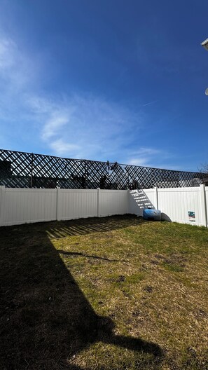 A fenced backyard with a white fence, a grassy area, and a clear blue sky.