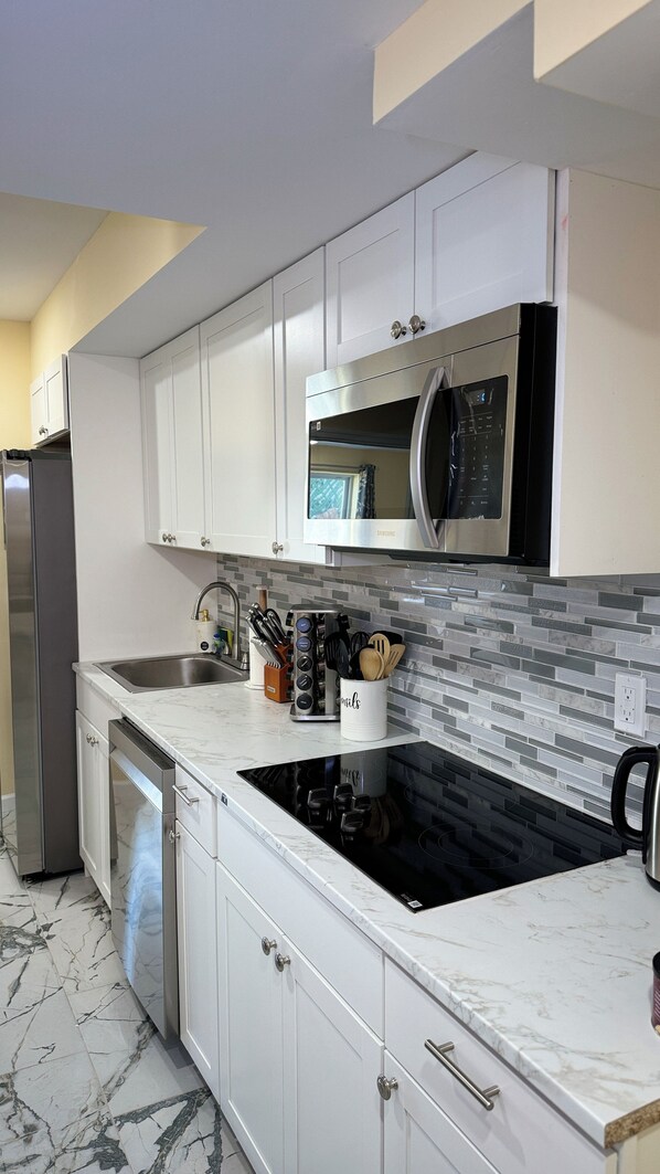 A modern kitchen with white cabinetry, a built-in microwave, a stainless steel refrigerator, and a black induction cooktop.
