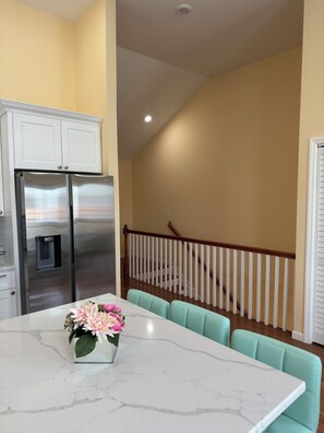 A kitchen with a stainless steel refrigerator, a marble countertop, and a dining area with teal chairs.