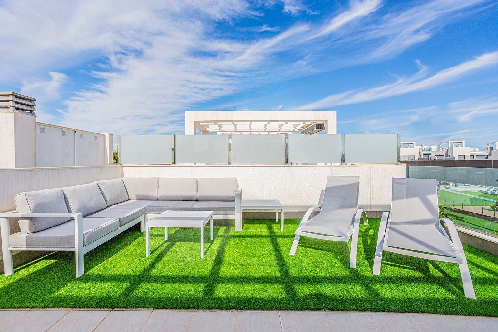 A rooftop terrace with a white sofa, two lounge chairs, and a small table.