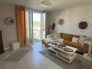 A living room with a sofa, coffee table, and a view through a sliding door to an outdoor area. - 2 bedrooms • Balcony with a view of Crussol • Near Valence (Guilherand-Granges)