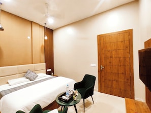 Habitación de hotel con cama, una pequeña mesa con silla, puerta de madera y ventilador de techo.