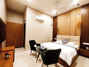 Quarto moderno com cama, duas cadeiras, uma mesa e aparelho de ar condicionado.