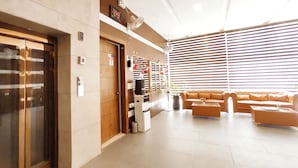 Et hotel lobby med receptionsdisk, sofa, skraldespand og loftventilator.