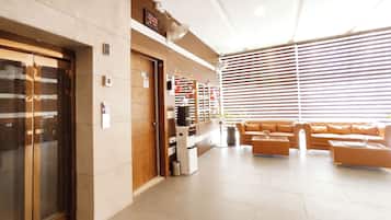 A hotel lobby with a reception desk, a sofa, a trash bin, and a ceiling fan.