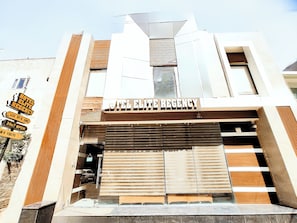 Un hôtel doté d’une façade moderne, d’une enseigne indiquant « HÔTEL ELITE REGENCY », et d’une entrée partiellement visible, avec un volet fermé.