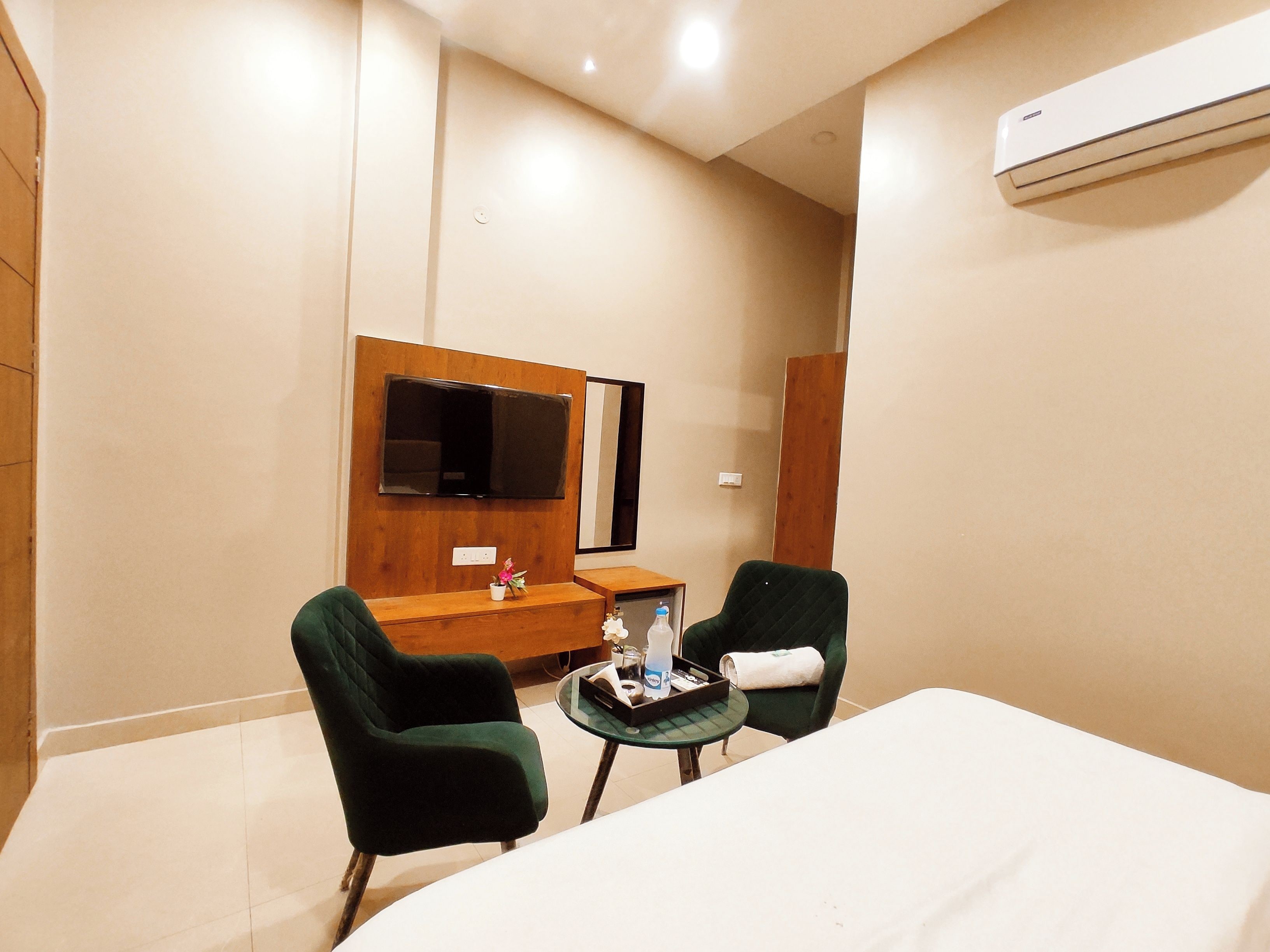 A hotel room with a bed, two chairs, a small table, a TV, and an air conditioning unit.