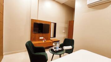A hotel room with a bed, two chairs, a small table, a TV, and an air conditioning unit.