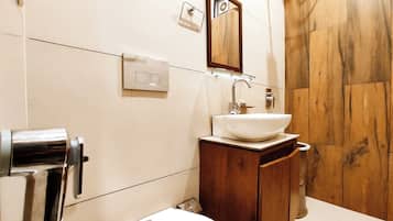 A bathroom with a wooden vanity, a white sink, a mirror, and a shower area.