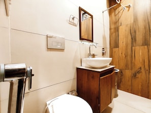 Un baño con tocador de madera, un lavabo blanco, un espejo y una zona de ducha.