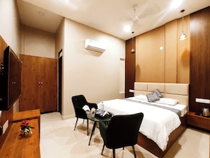 Habitación de hotel con cama, escritorio, silla, televisor y armario.
