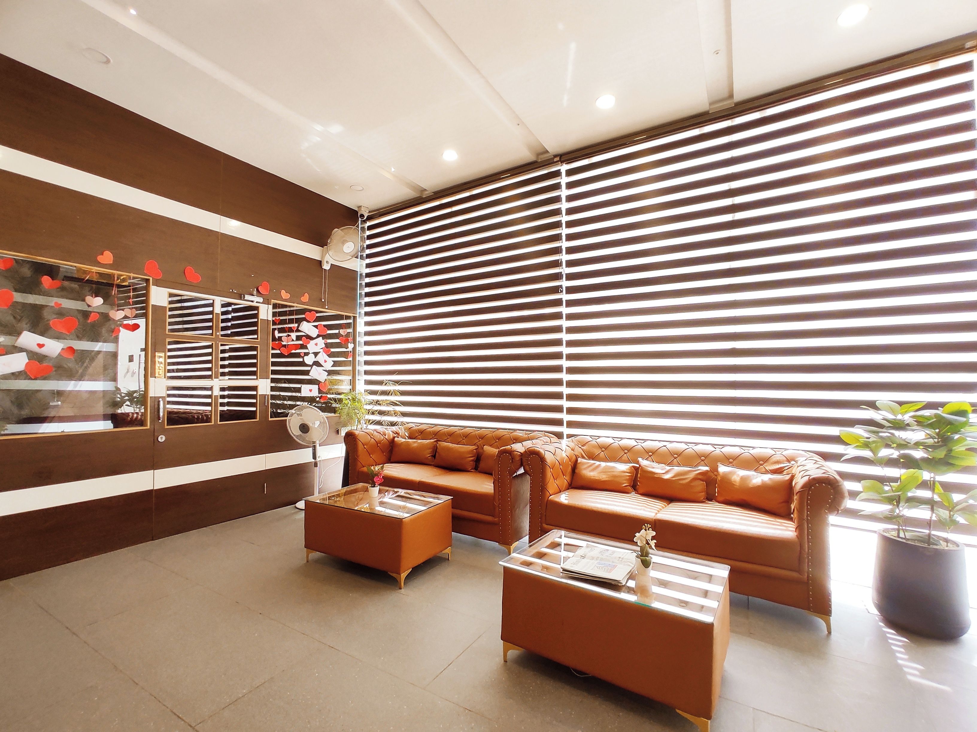 Un salon moderne avec un canapé en cuir marron, une table basse en verre et une grande fenêtre dotée de stores horizontaux.