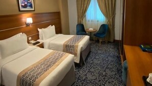 Camera d'albergo con due letti, una scrivania, una sedia, una finestra con tende e una testiera.