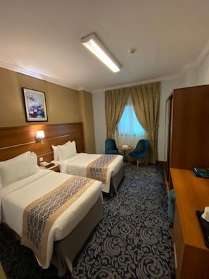 Habitación de hotel con dos camas, un escritorio, una silla, un ventanal con cortinas y un cabecero.