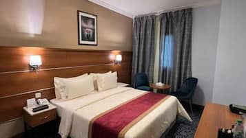 A hotel room with a bed, bedside tables, a desk, and a chair.