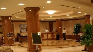 Una hall d'albergo con reception, area salotto e una grande pianta.