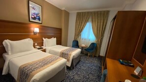 Una camera d'albergo con due letti, una scrivania, una sedia, un tavolino e una finestra con tende.
