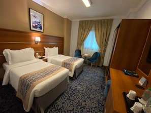 Habitación de hotel con dos camas, un escritorio, una silla, una mesita y una ventana con cortinas.