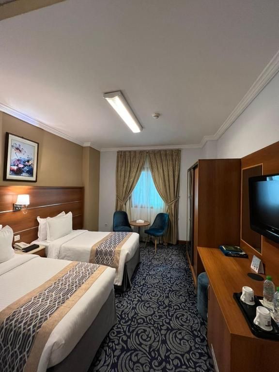 A hotel room with two beds, a desk with a television, a small table, and a chair.