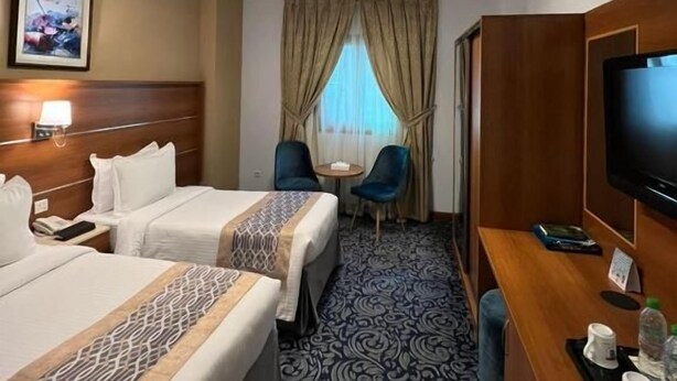 Una camera d'albergo con due letti, una scrivania con televisore, un piccolo tavolo e una sedia.