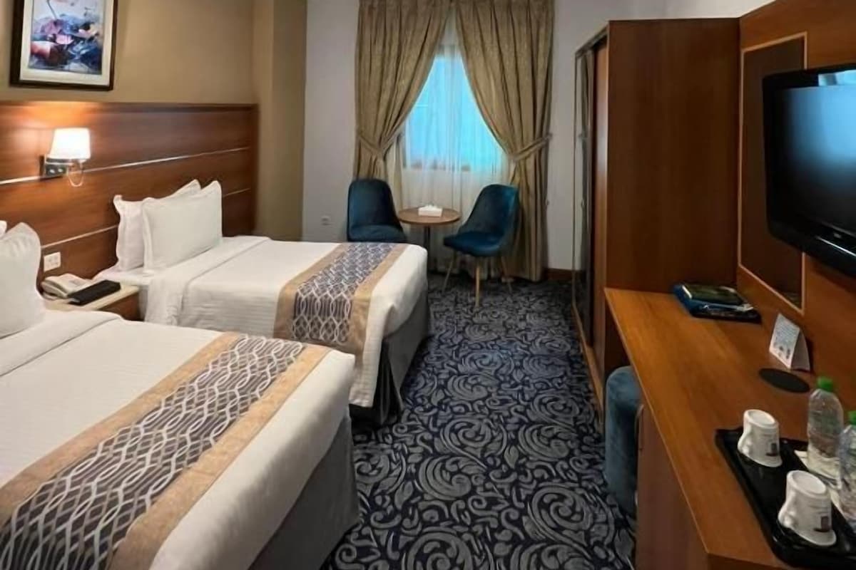 Habitación de hotel con dos camas, un escritorio con televisor, una mesita y una silla.