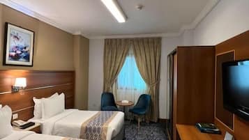 A hotel room with two beds, a desk with a television, a small table, and a chair.