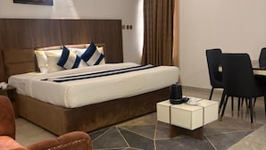 A hotel room with a bed, a desk, a chair, a coffee table, and a wall-mounted air conditioner. - Merat Hotel And Suites (Jimeta)