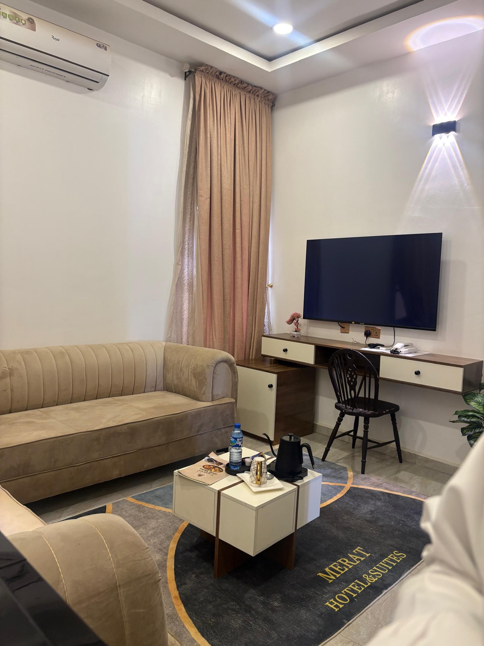 A hotel room with a sofa, a desk with a computer, a TV, and a coffee table.