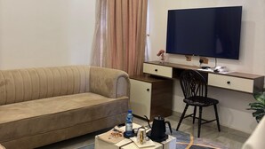 A hotel room with a sofa, a desk with a computer, a TV, and a coffee table. - Merat Hotel And Suites (Jimeta)