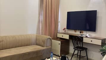 A hotel room with a sofa, a desk with a computer, a TV, and a coffee table.