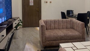 A modern room with a sofa, a television, a desk with a computer, and a 'NO SMOKING' sign on the door. - Merat Hotel And Suites (Jimeta)