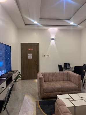 A modern room with a sofa, a television, a desk with a computer, and a 'NO SMOKING' sign on the door. - Merat Hotel And Suites (Jimeta)