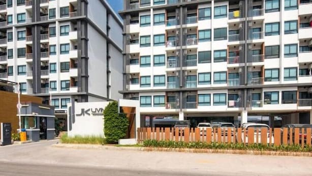 Un edificio residencial de varios pisos con balcones, un acceso con portón y una zona de estacionamiento.