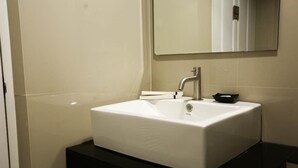 Un baño con lavamanos blanco, espejo y encimera negra.
