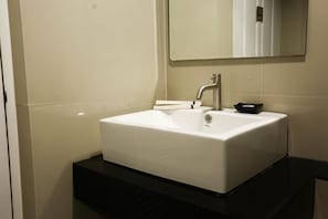 Casa de banho com lavatório branco, espelho e bancada preta.
