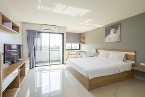 Quarto de hotel moderno com uma cama grande, televisão, escrivaninha e varanda com cortinas.
