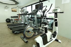 Ginásio com diversos equipamentos de exercício, incluindo esteiras, um elíptico e uma bicicleta ergométrica.