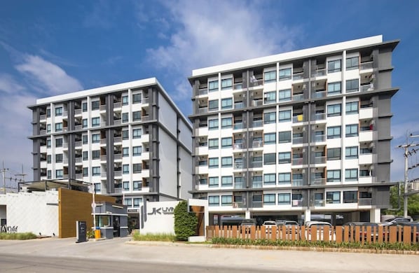 A multi-story residential building with balconies, a gated entrance, and a parking area. - Jk Living Hotel And Service Apartment (Chachoengsao)