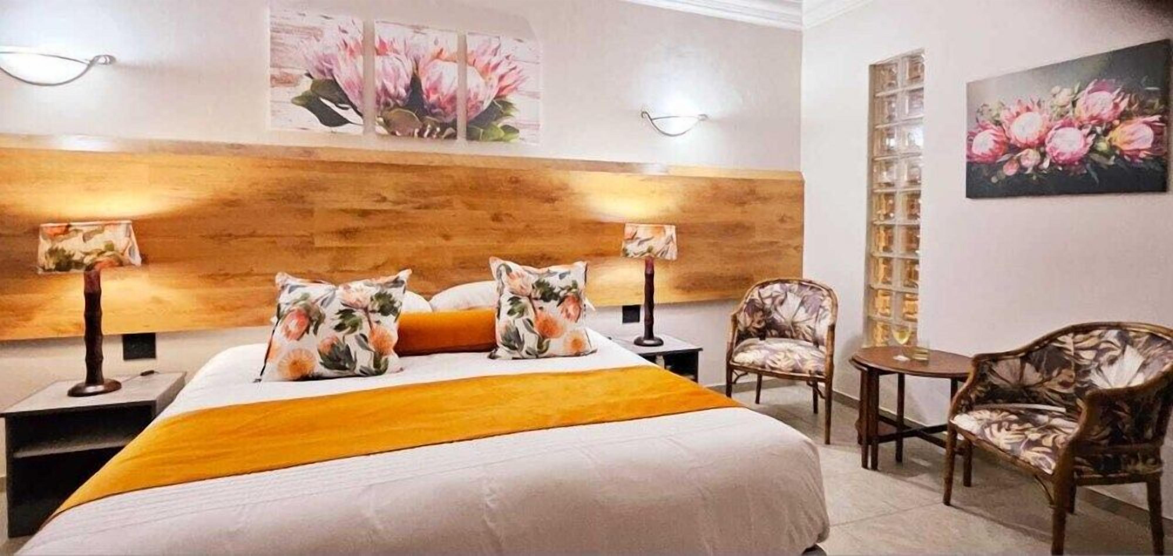 A hotel room with a bed, two nightstands, a chair, a small table, and wall-mounted lamps.