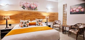 Una habitación de hotel con una cama, dos mesitas de noche, una silla, una pequeña mesa y lámparas de pared.