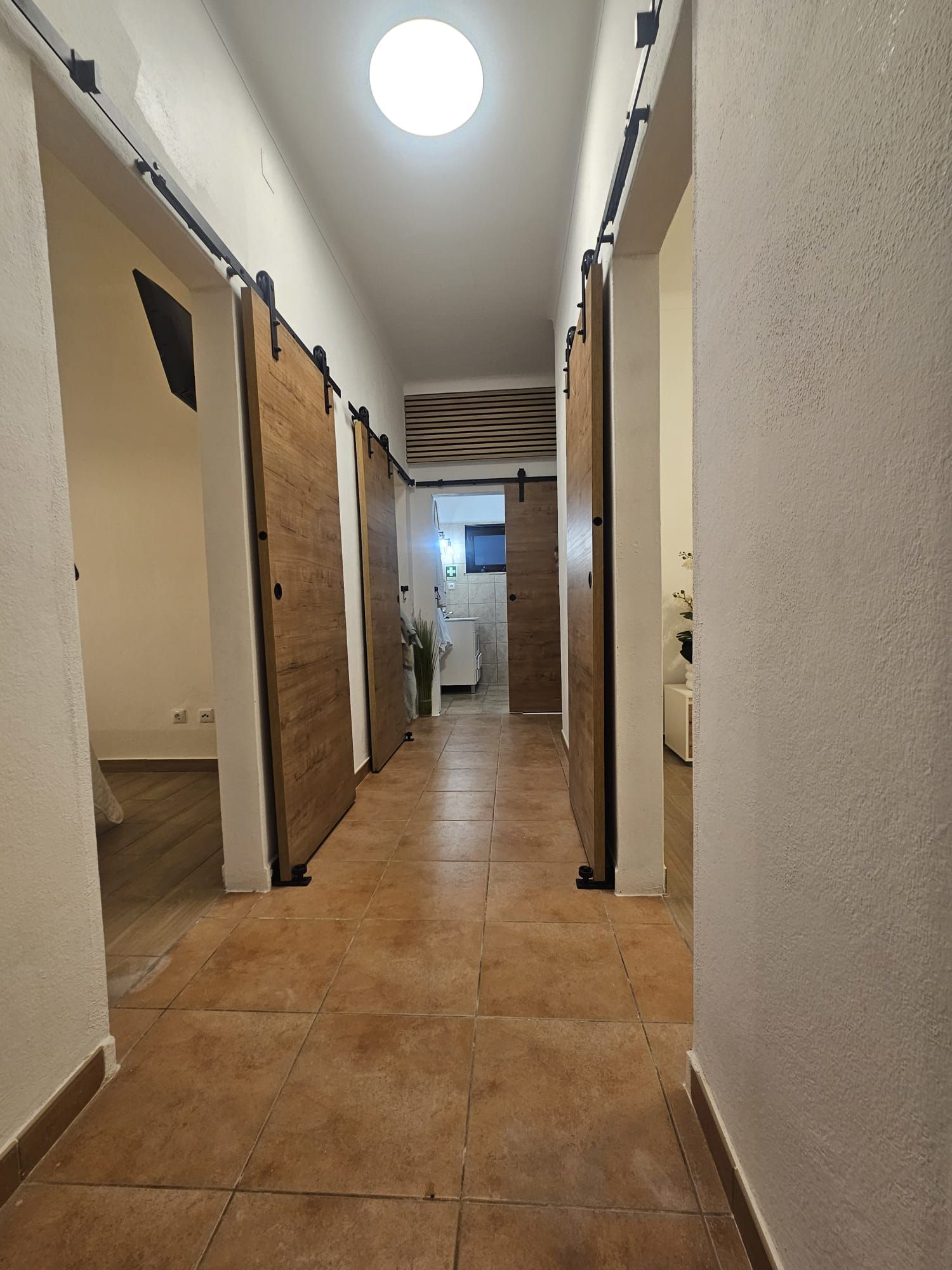 A hallway with a tiled floor, wooden doors, and a ceiling light.