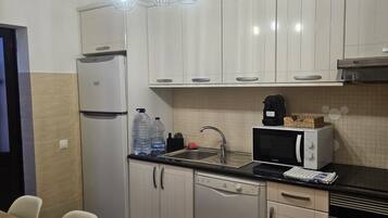 A compact kitchen with white cabinets, a refrigerator, a dishwasher, a microwave, and a coffee maker.