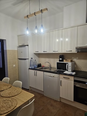 Una cuina compacta amb armaris blancs, nevera, rentaplats, microones i cafetera.